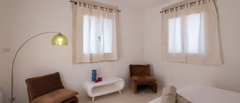 Una habitación de hotel con una cama, dos sillones marrones, una mesita blanca con adornos y una lámpara de pie.