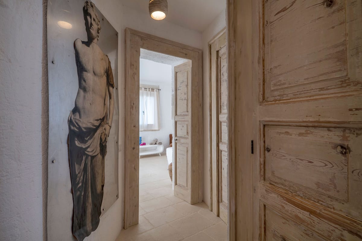 Ein Flur mit einer großen Skulptur, Holztüren und einem Blick in ein Schlafzimmer mit Bett und Vorhängen.