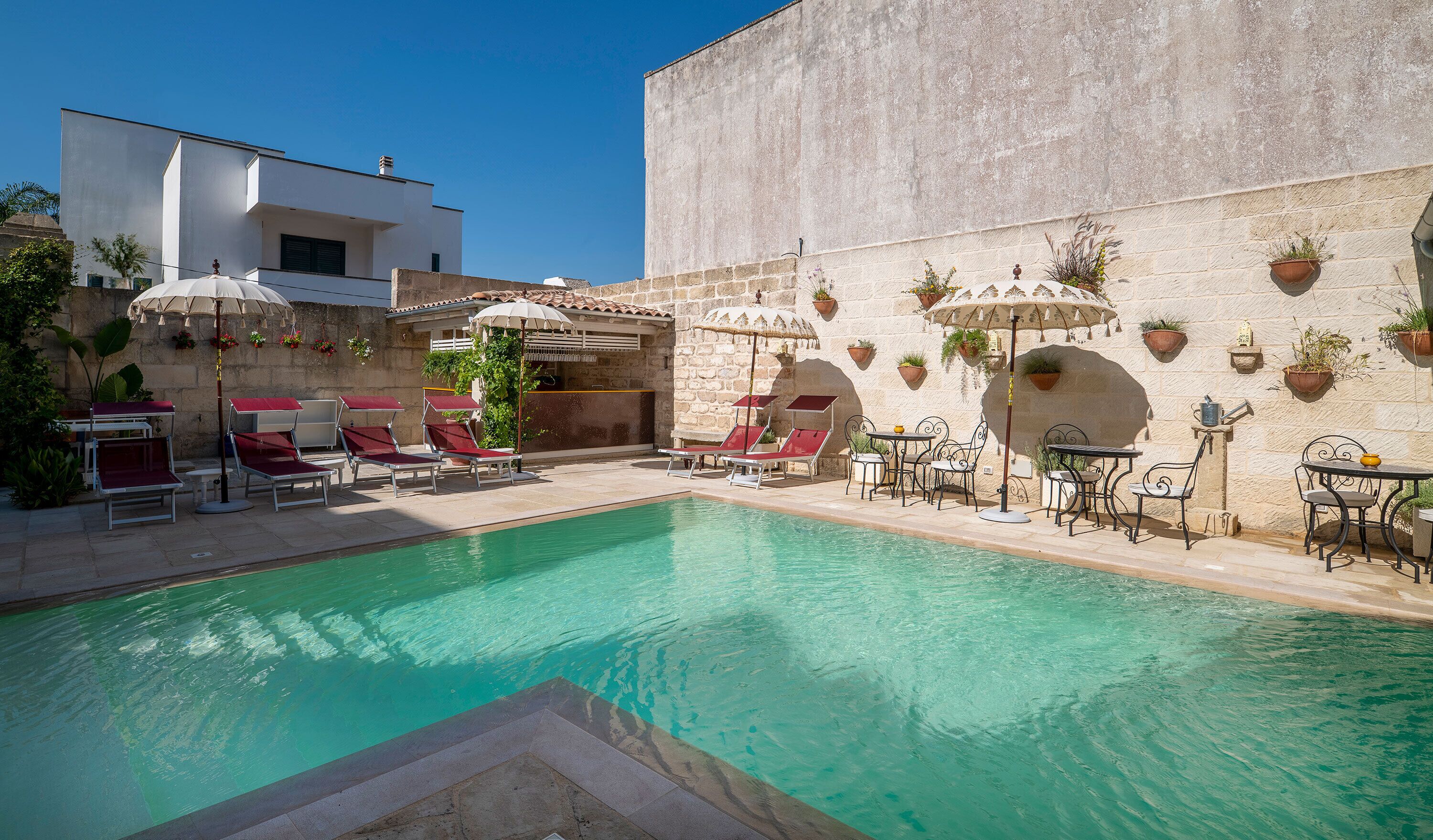 A poolside area with lounge chairs, umbrellas, and potted plants.