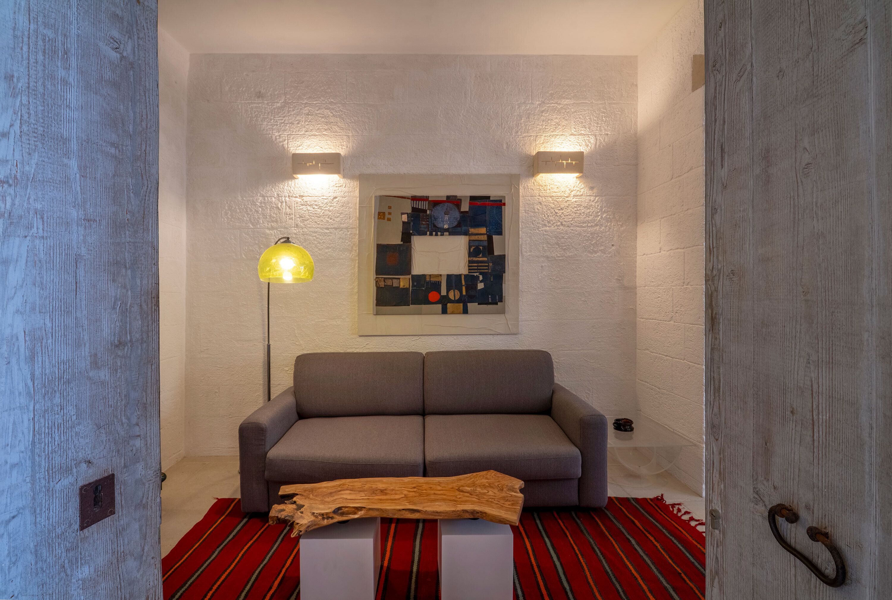 Ein modernes Wohnzimmer mit grauem Sofa, einem Holztisch, einem Teppich in Rot und Schwarz gestreift sowie einem Wandbild.