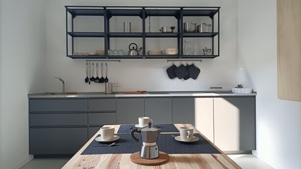 A modern kitchen with a built-in shelf unit above the countertop, a coffee maker on the table, and a kettle hanging on the wall. - Bed and Bike Hostel  (San Giovanni in Persiceto)