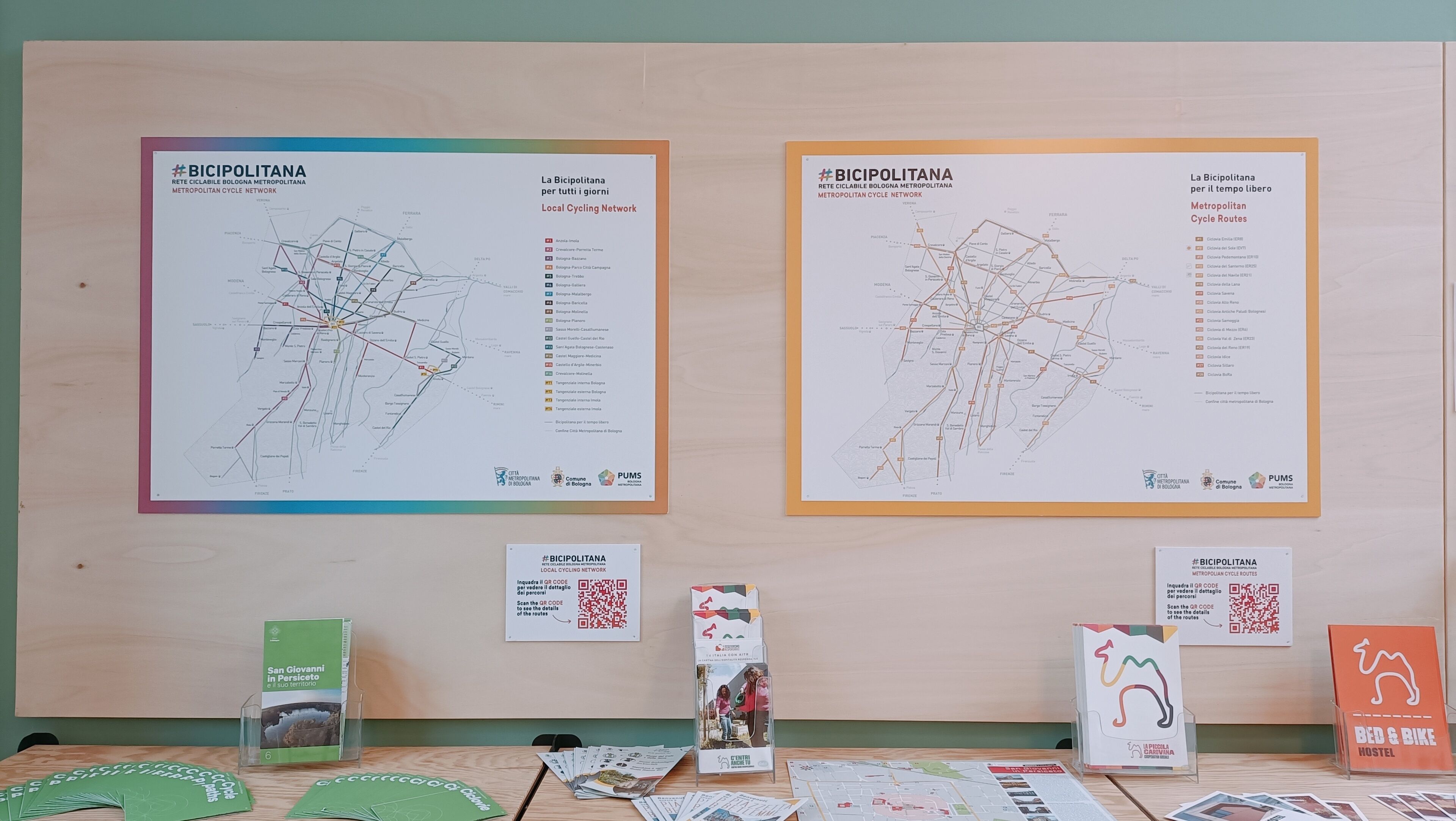 Dois mapas grandes da rede Bicipolitan em uma parede, com folhetos informativos e códigos QR abaixo.