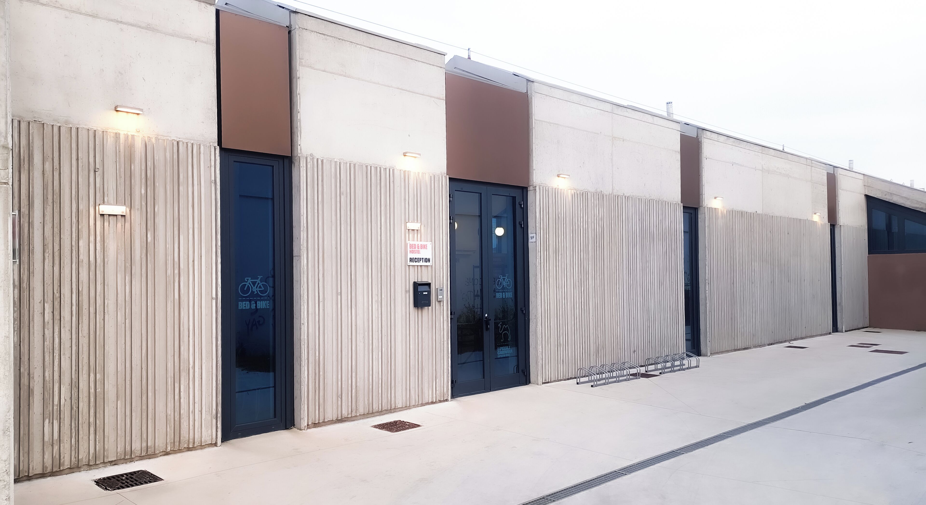 Un edificio moderno con zona de recepción, espacio para guardar bicicletas y un cartel que indica un albergue de camas y bicicletas.