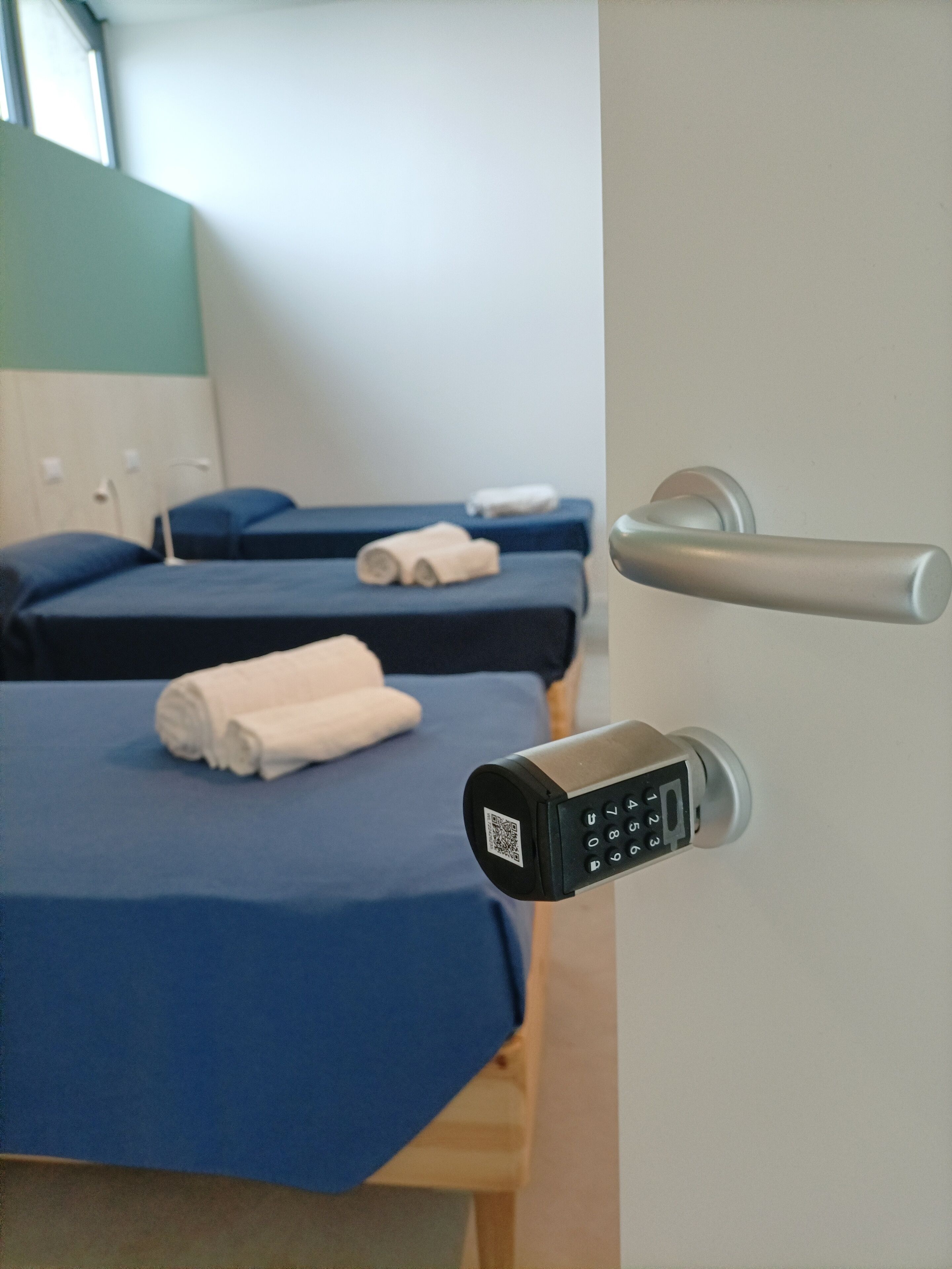 Habitación de hotel con cama, mesita de noche y puerta con cerradura electrónica.