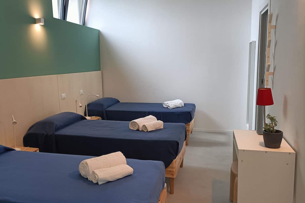 A hotel room with two beds, each with a blue bedspread and white towels. There is a small table with a potted plant and a red lamp.