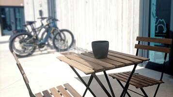 Un espace extérieur aménagé avec une table en bois et des chaises en métal, un vélo garé au fond, et un bâtiment sur lequel on peut lire l’inscription « ED & BIKE ».