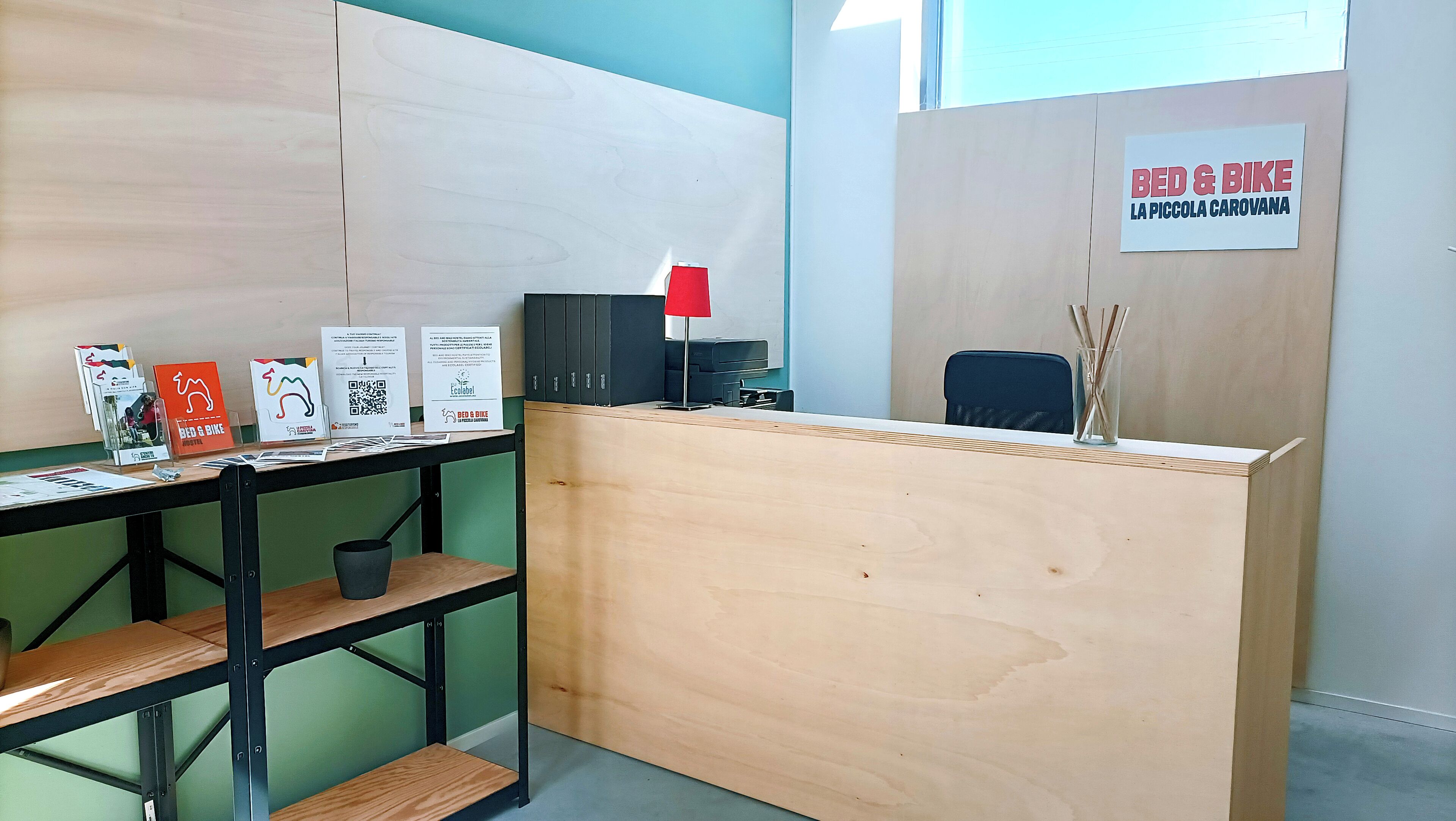 A reception desk with a sign reading "BED & BIKE LA PICCOLA CAROVANA".