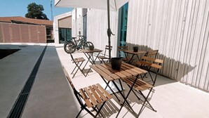 An outdoor seating area with wooden tables and benches, a bicycle parked against a wall, and a white awning providing shade. - Bed and Bike Hostel  (San Giovanni in Persiceto)