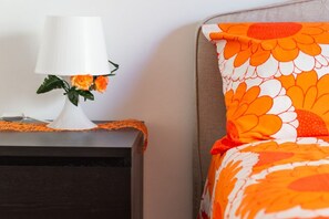A bed with a floral-patterned pillow and a white lamp with flowers on a bedside table. - Camera Augusto 42 By Dimorra (NAPOLI)