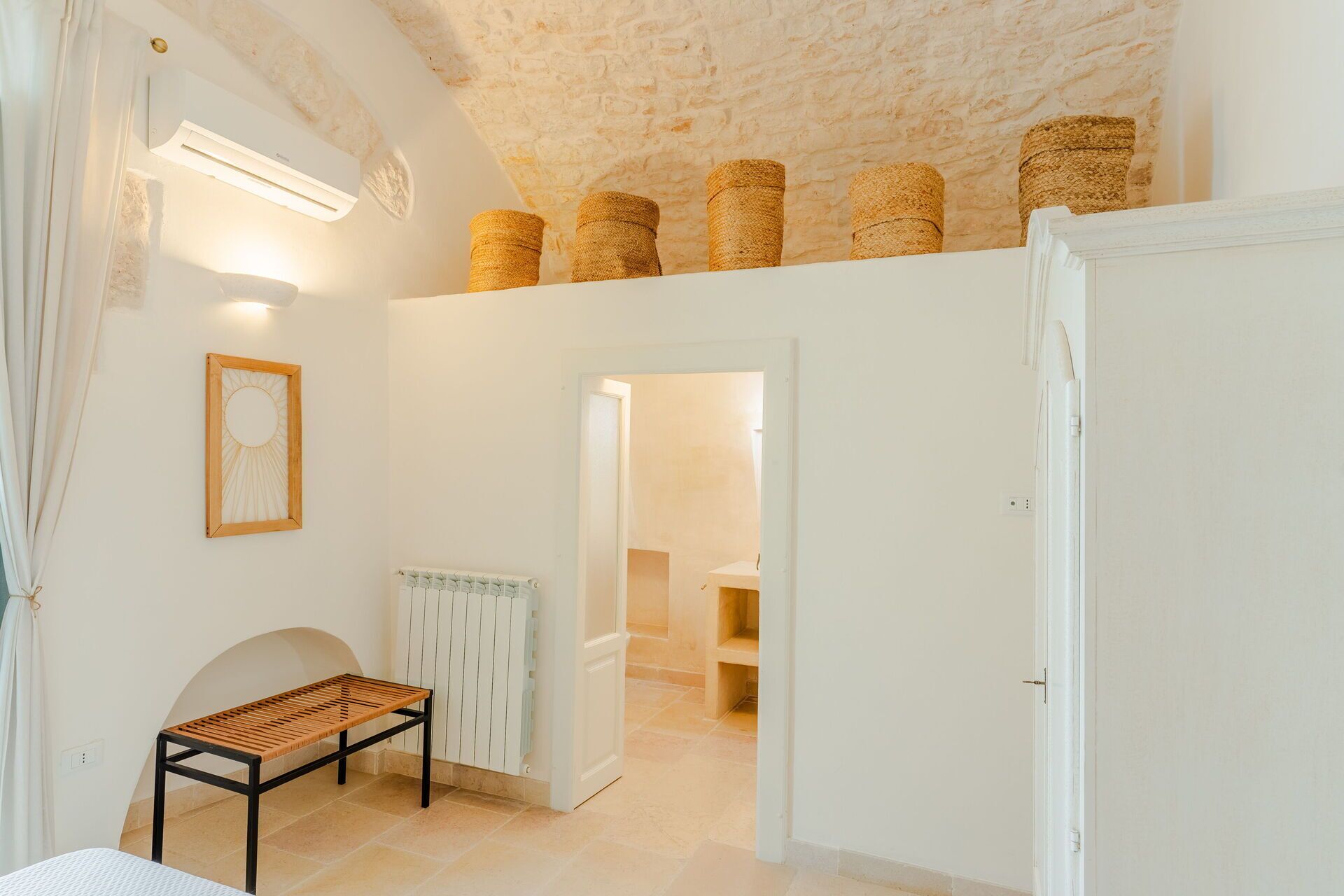 Une pièce avec un plafond haut, un banc en bois, un radiateur et une porte donnant sur une autre pièce.
