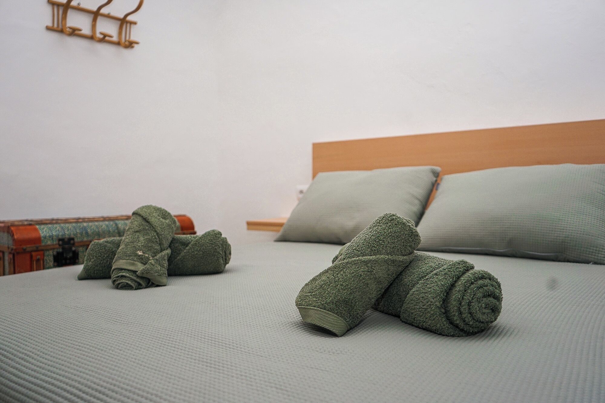 Un lit bien fait, avec des serviettes vertes, une tête de lit en bois et un crochet fixé au mur.