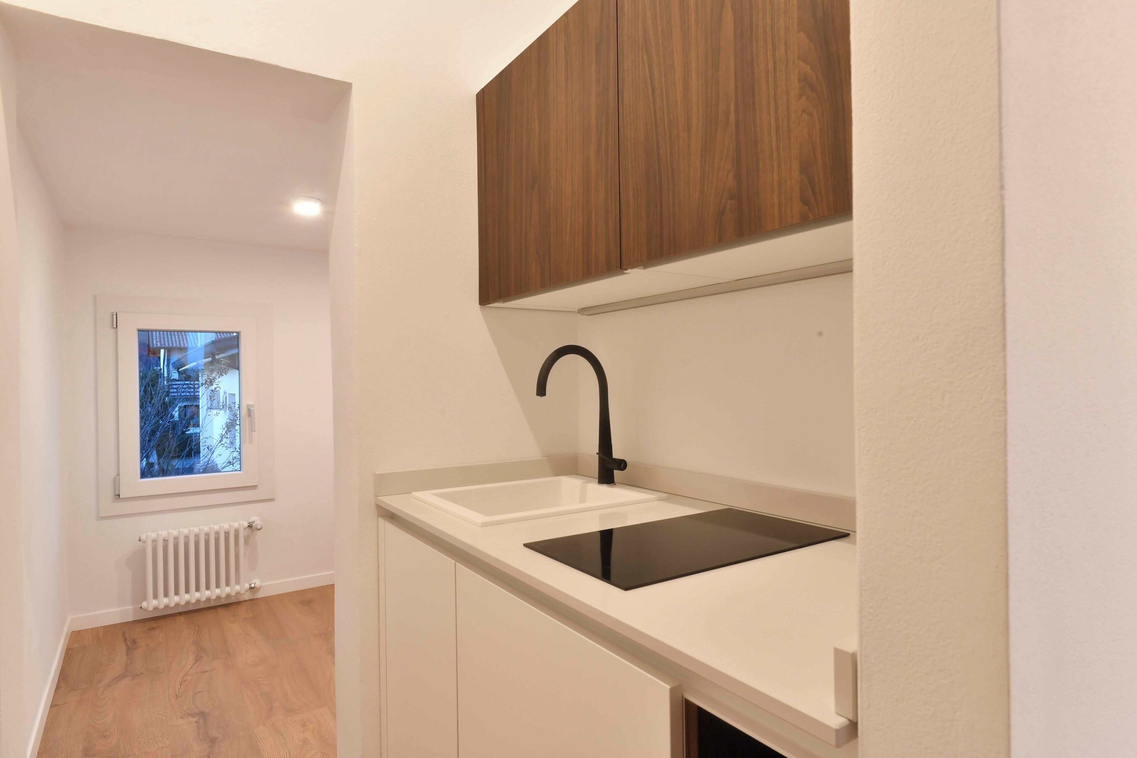 Una piccola cucina con un piano di lavoro bianco, un lavandino nero e mobili in legno.