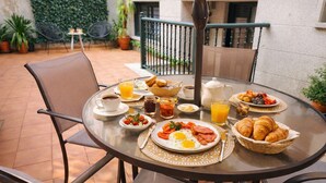 A round dining table with breakfast items, chairs, and a view of a garden and building in the background.
