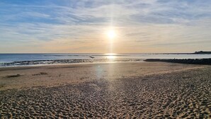 A beach with a clear sky and the sun low on the horizon.