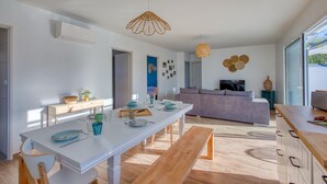 A modern living room with a white sofa, a dining table with chairs, and a kitchen area with a bench.