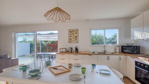 A modern kitchen with white cabinets, a large island with dining set, and a view of the garden through the sliding doors.