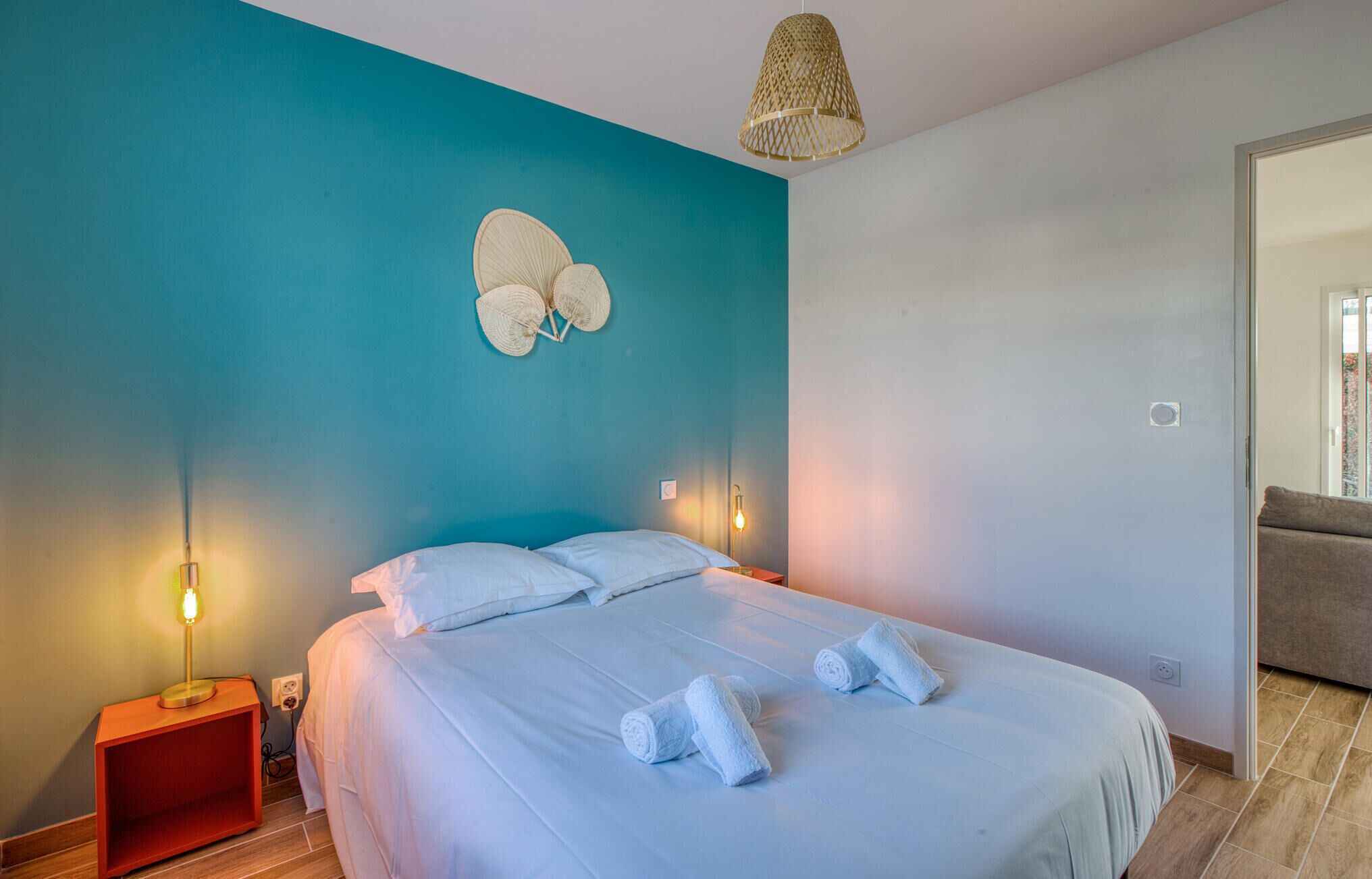 A bedroom with a bed, two bedside lamps, a wall-mounted light fixture, and a door leading to another room.