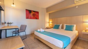 Hotelkamer met een bed, een bureau, een stoel, een tafel, een wandairconditioner en een schilderij.