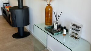 Una sala de estar moderna con una estufa de leña negra, una mesa de centro de cristal y elementos decorativos, incluyendo un jarrón con plumas de pampa y una botella de perfume.