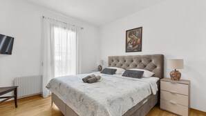 Une chambre à coucher avec un lit, une table de chevet, une lampe, un tableau et une fenêtre avec des rideaux.