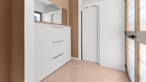 Un couloir avec une armoire blanche, une porte dotée d’une poignée et un sol carrelé.