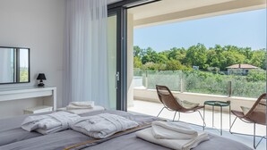 Ett modernt hotellrum med en stor säng, ett skrivbord och en balkong med flätade fåtöljer och ett bord.