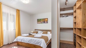 Quarto com cama de madeira, roupa de cama branca, um quadro na parede e um guarda-roupa de madeira.