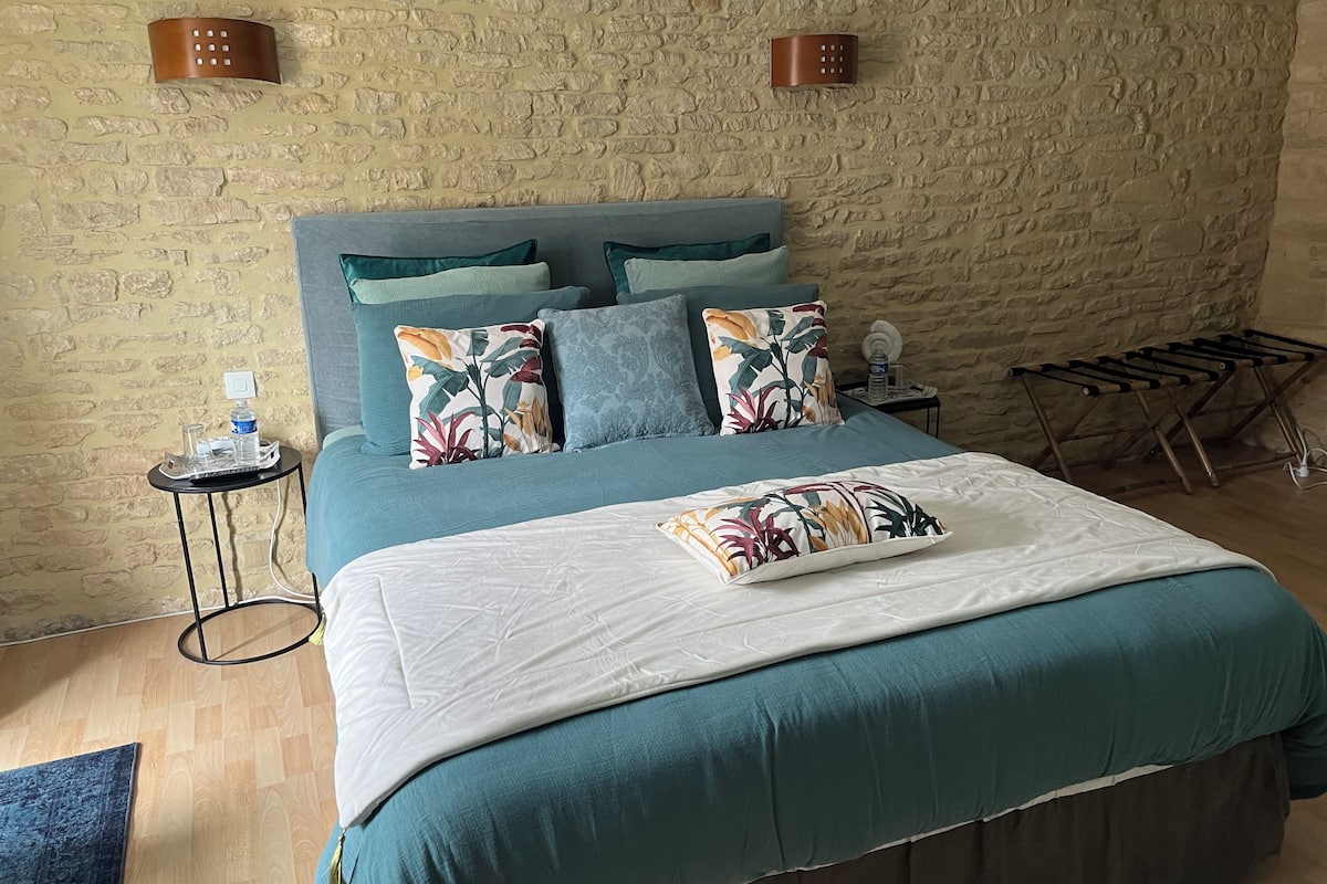 Une chambre à coucher avec un lit, des oreillers, une table de chevet, une lampe fixée au mur et un étendoir.
