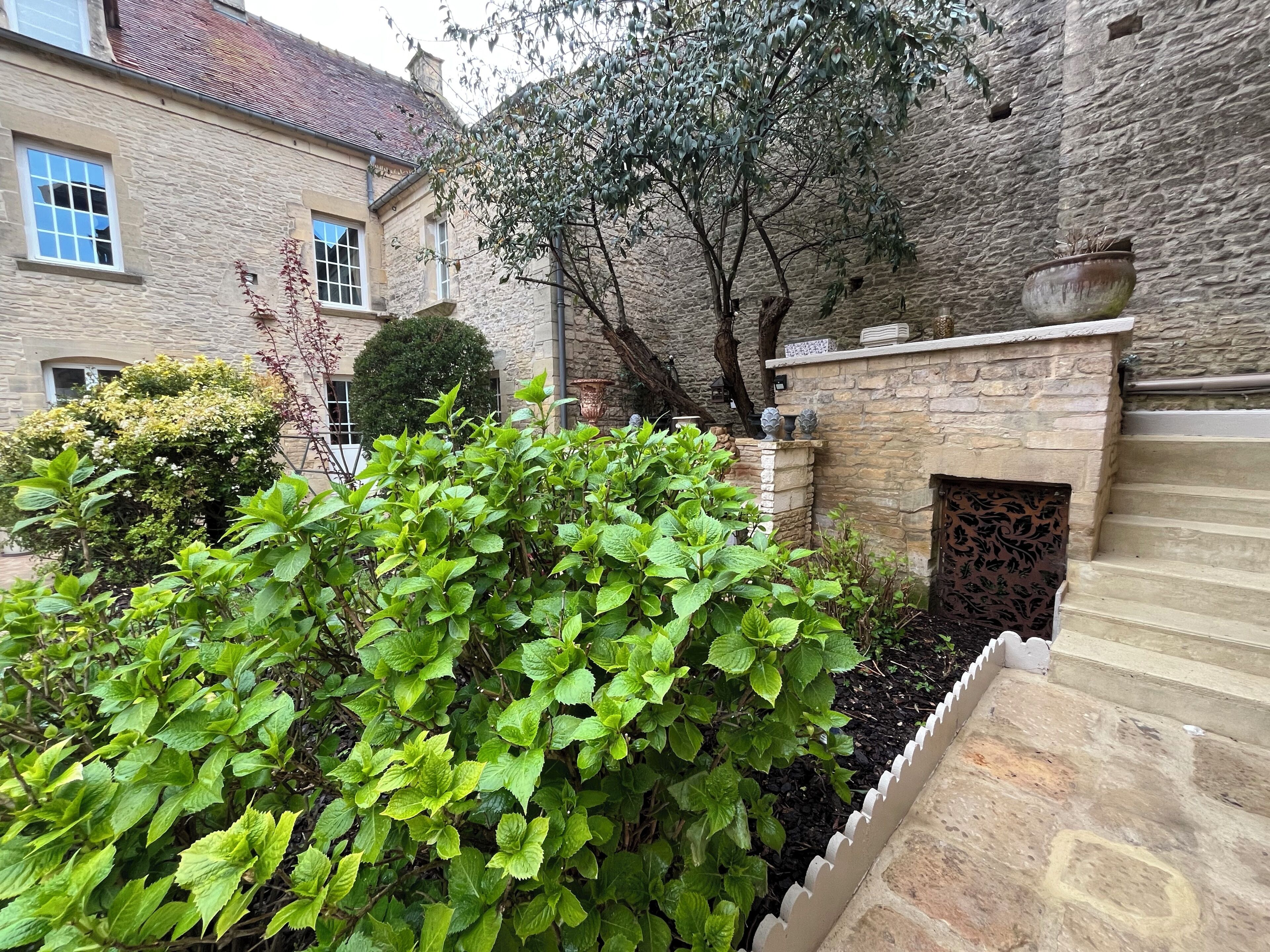 Un bâtiment en pierre doté d’un jardin, d’un petit arbre et d’un mur décoratif.