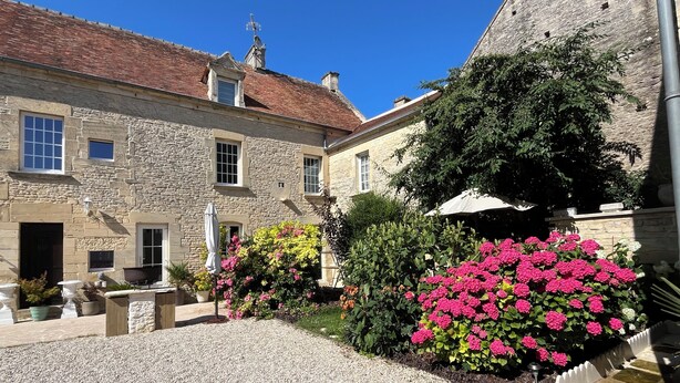 A stone building with a gravel courtyard, potted plants, and a clear blue sky. - Chambres d'Hôtes de l'Ancienne Auberge (Thaon)