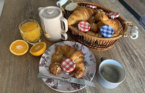 A breakfast setting with a croissant, orange slices, a teapot, a cup of coffee, and a basket of pastries. - Chambres d'Hôtes de l'Ancienne Auberge (Thaon)