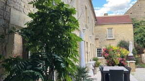 A courtyard with stone buildings, a table with chairs, and potted plants. - Chambres d'Hôtes de l'Ancienne Auberge (Thaon)