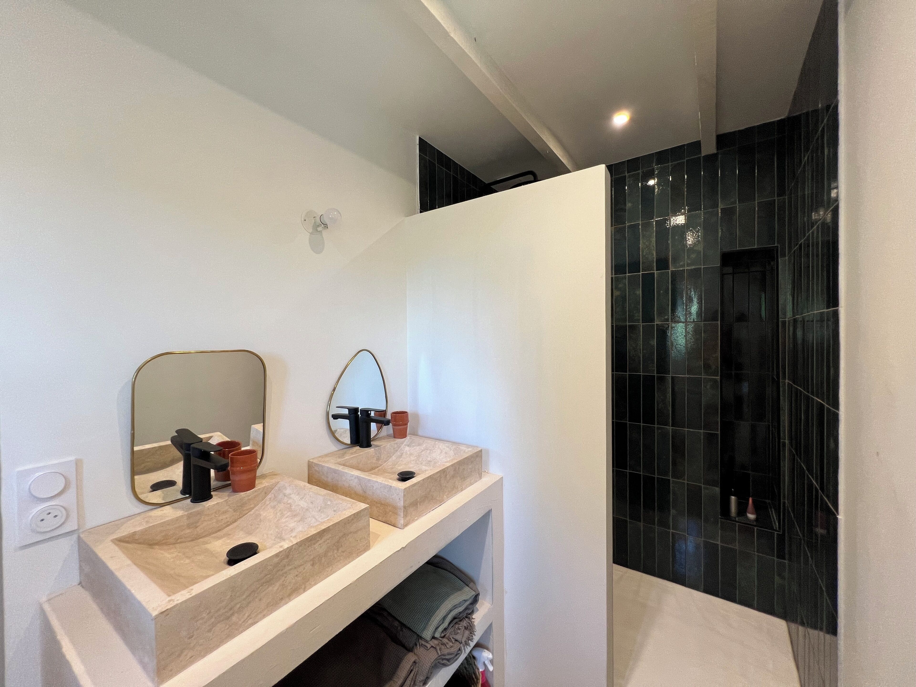 A modern bathroom with two sinks, a large mirror, and black tiled walls.