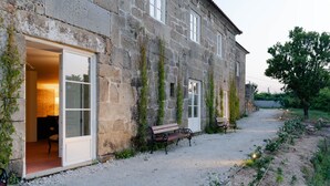 A stone building with a bench in front, a gravel path, and a garden area.