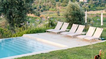A poolside area with lounge chairs and a view of a hillside.