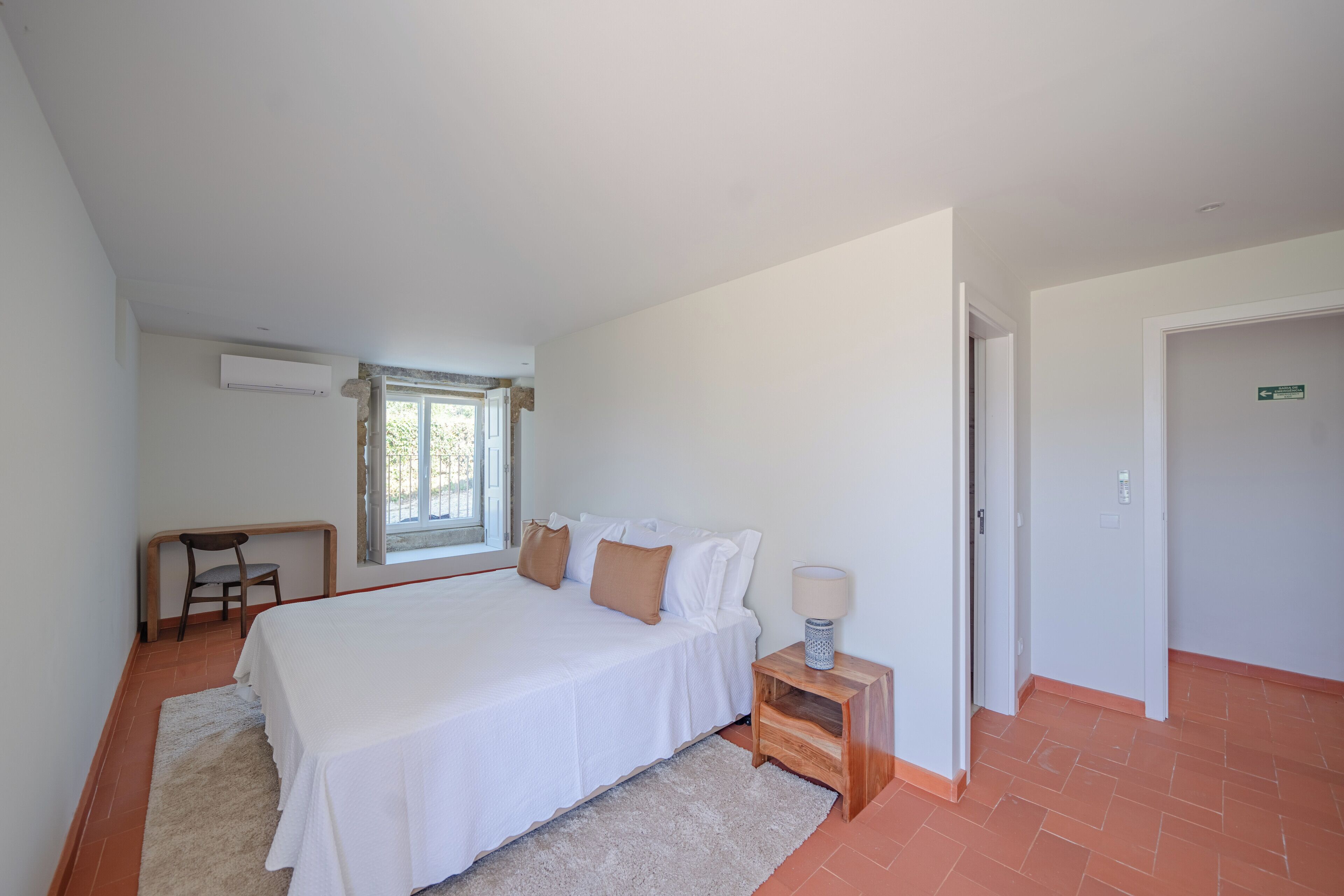 Een slaapkamer met een groot bed, een nachtkastje met een lamp, een stoel en een raam.