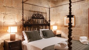 A four-poster bed with a wooden headboard, two bedside tables with lamps, and a stone wall.