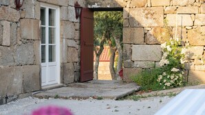 A stone building with a white door and a red door, a stone wall, and a small garden with white flowers.