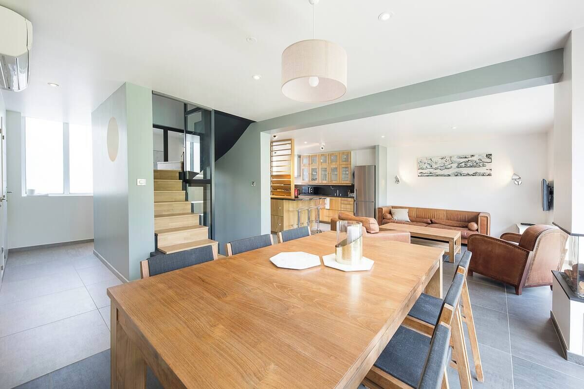 Een modern interieur met een houten eettafel, een bank en een trap naar een verdieping erboven.