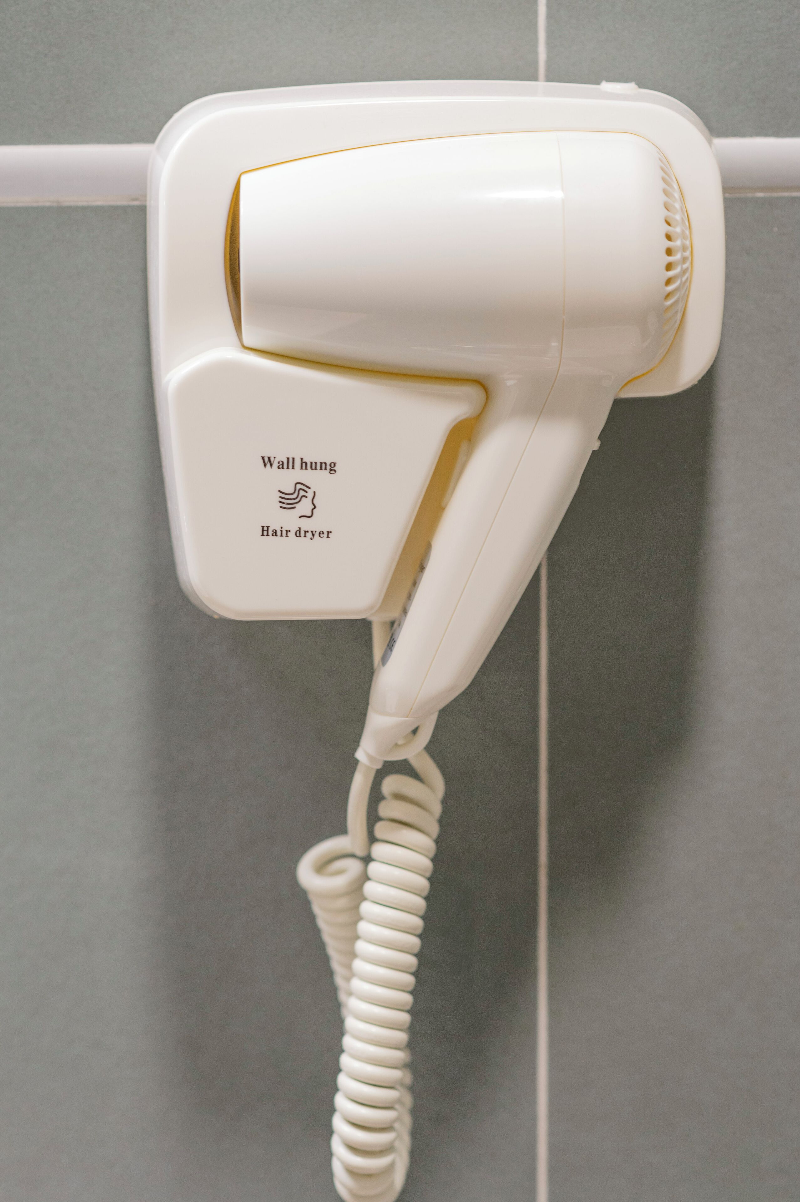 A wall-mounted hair dryer with a coiled cord.