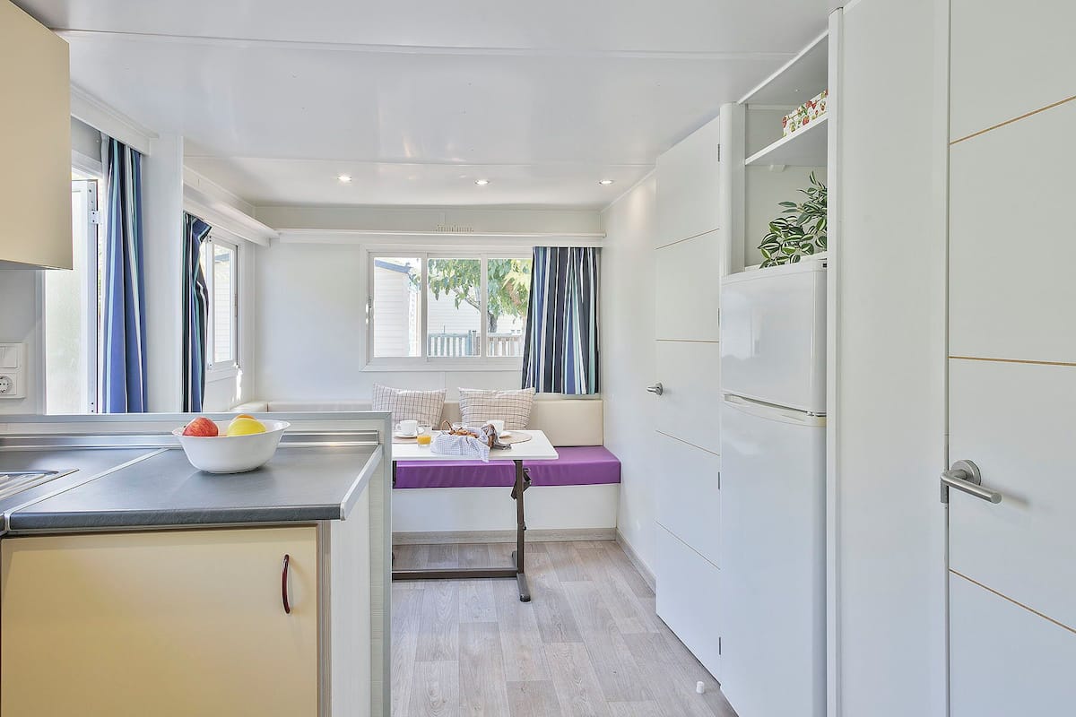 Cocina compacta con zona de comedor, una ventana con cortinas y un refrigerador.