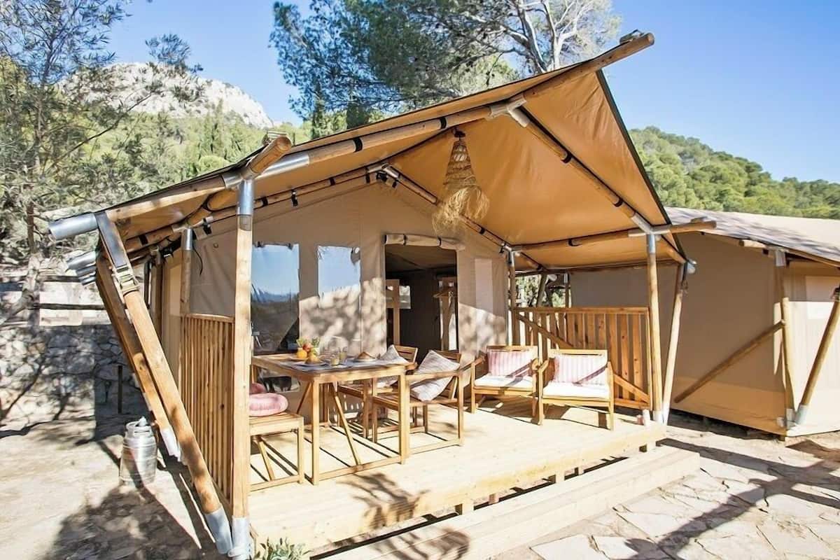 Una carpa de madera con una mesa y sillas, con montañas al fondo.