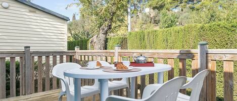 A deck with a round table and white plastic chairs, a teapot, and a croissant on the table.