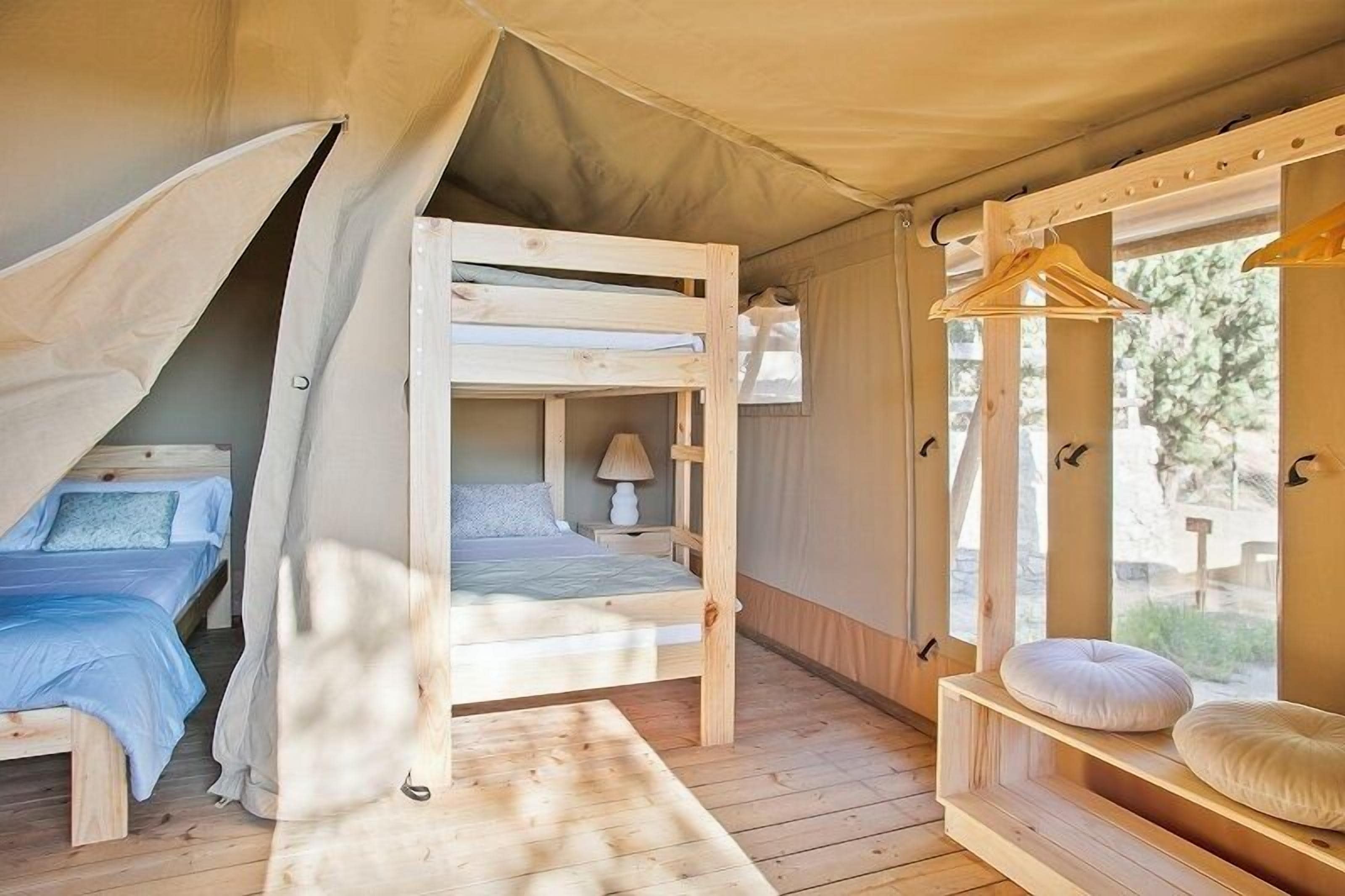 A cozy tented accommodation with two bunk beds, a small table, and a hanging clothes rack.