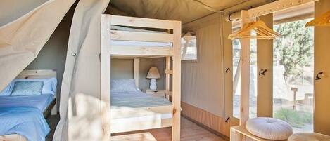 A cozy tented accommodation with two bunk beds, a small table, and a hanging clothes rack.