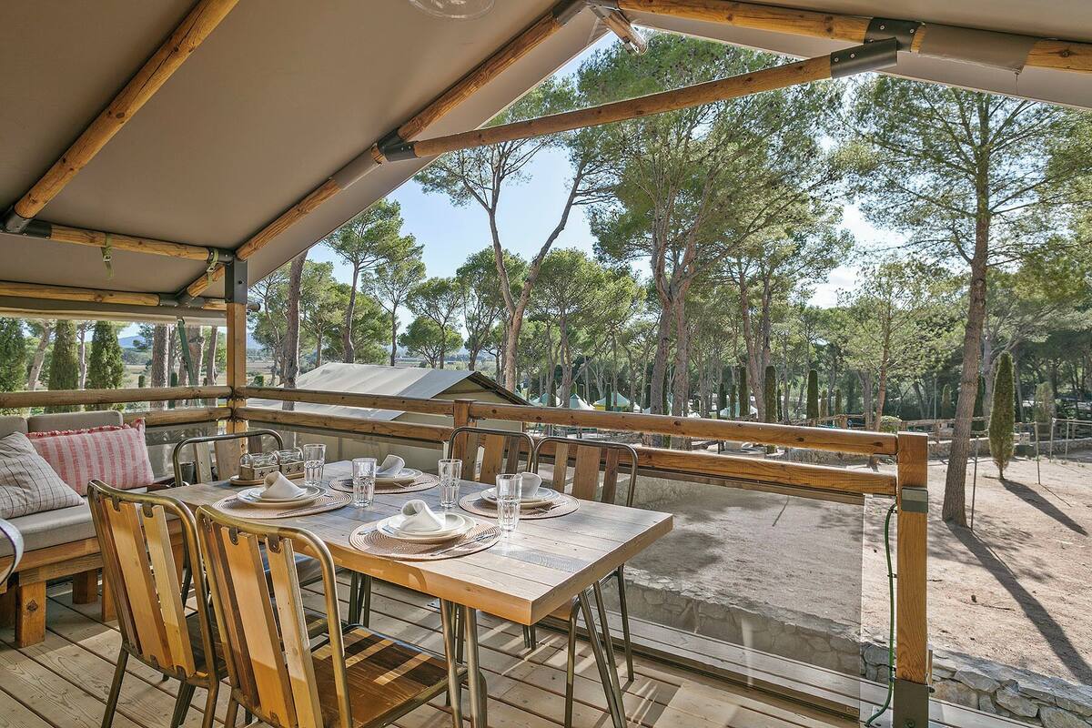 Un área de comedor al aire libre con una mesa lista para dos personas, rodeada de sillas de madera y una terraza de madera.