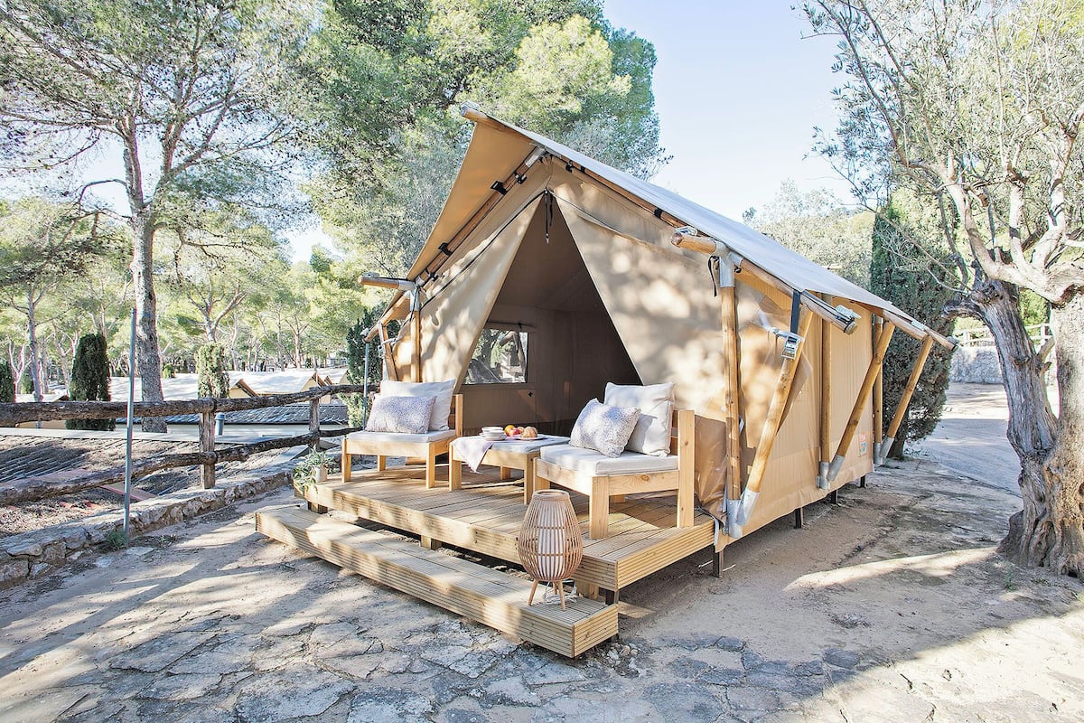 Una tienda acogedora de una sola habitación con terraza de madera y una pequeña mesa, rodeada de árboles.
