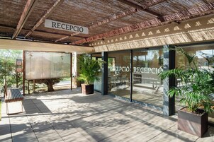Una zona de recepción con un letrero que dice "RECEPCIÓN", ventanas amplias, plantas en macetas y suelo de baldosas.