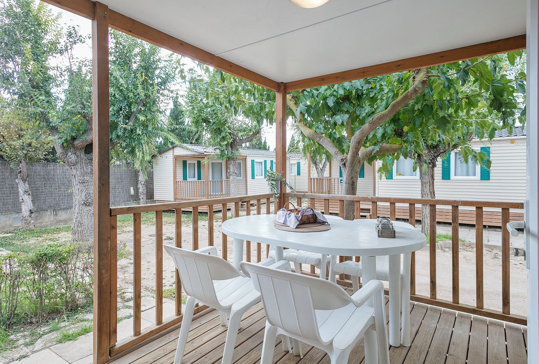 A covered outdoor seating area with a table and chairs, surrounded by wooden railings and trees.