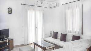 A living room with a sofa, a coffee table, a TV, and curtains. - Villa Elena Glysteri (Skopelos)